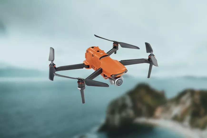 An orange drone flying over a mountain.