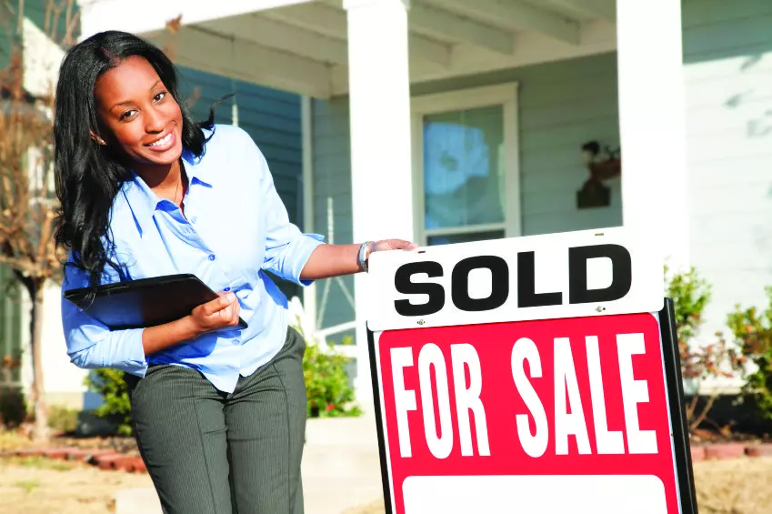 black realtor holding for sale sign in front of house