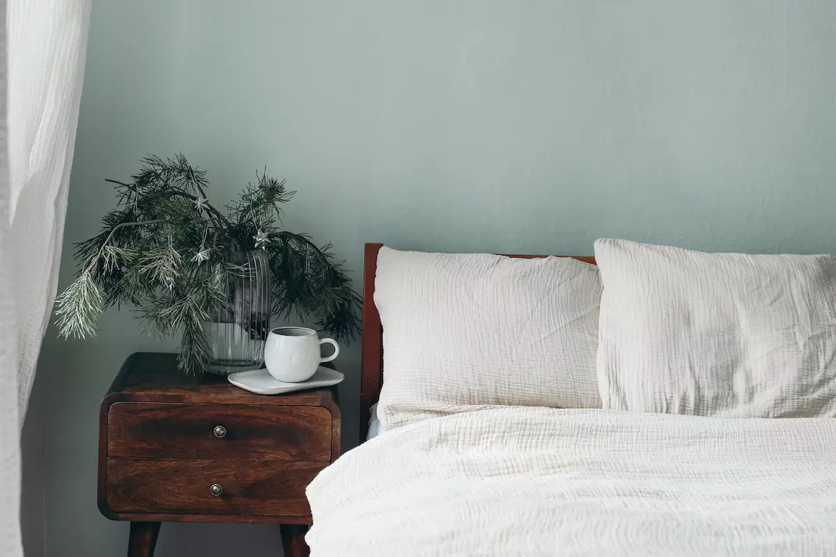 Close up of a bed with white sheets against light green walls