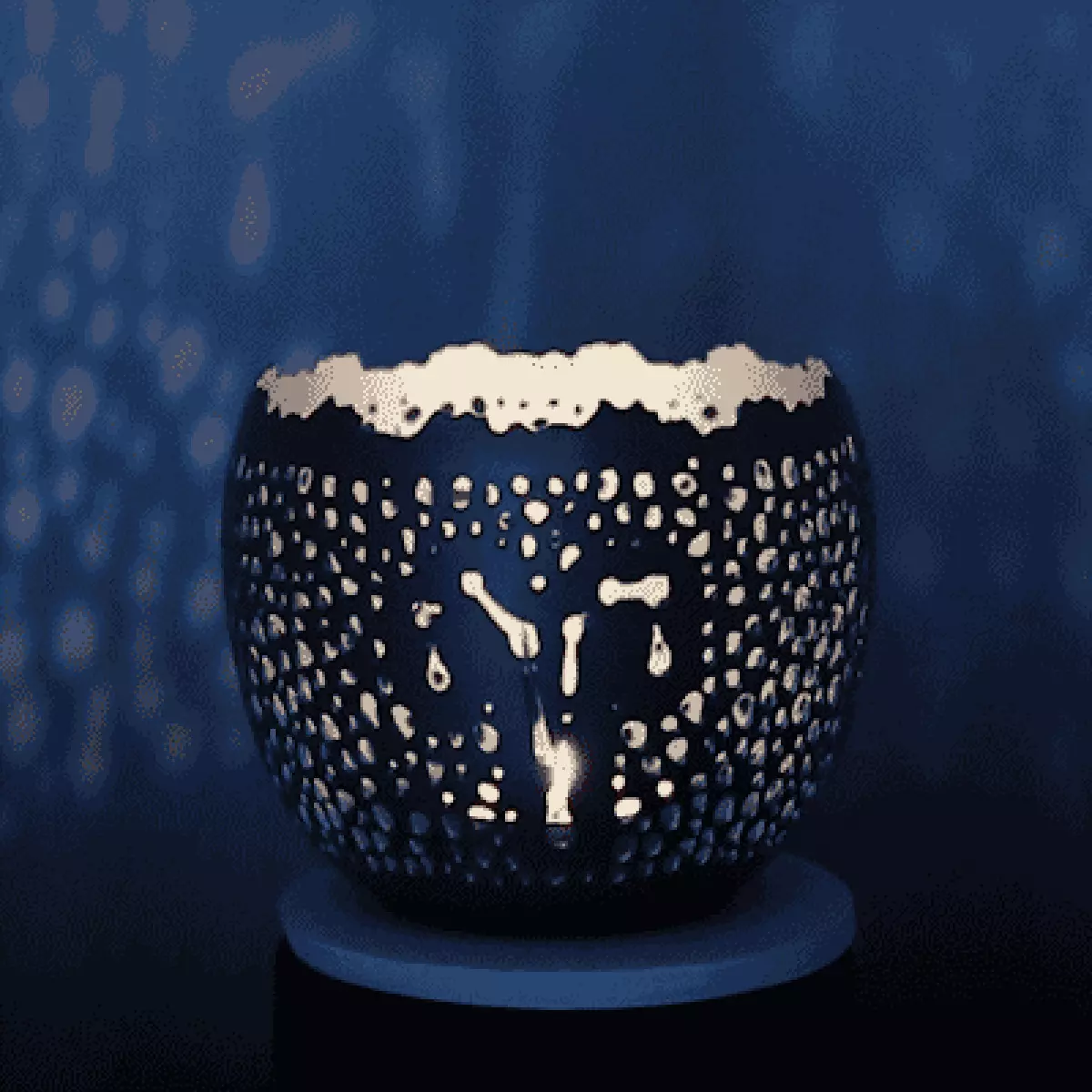 Gif of fair trade, handcrafted Zodiac candleholder with the Aries sign in the punchwork spinning slowly; casting light patterns on the indigo walls around it.