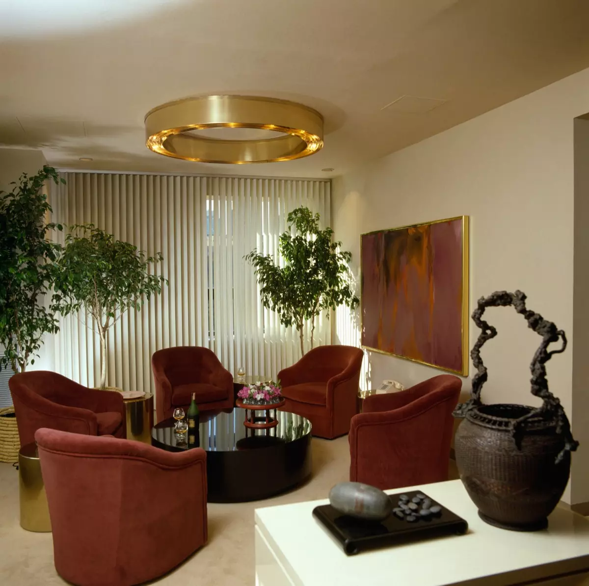 A9K1RP Circular metal light fitting in eighties living room with red velour sofas and vertical Venetian blinds