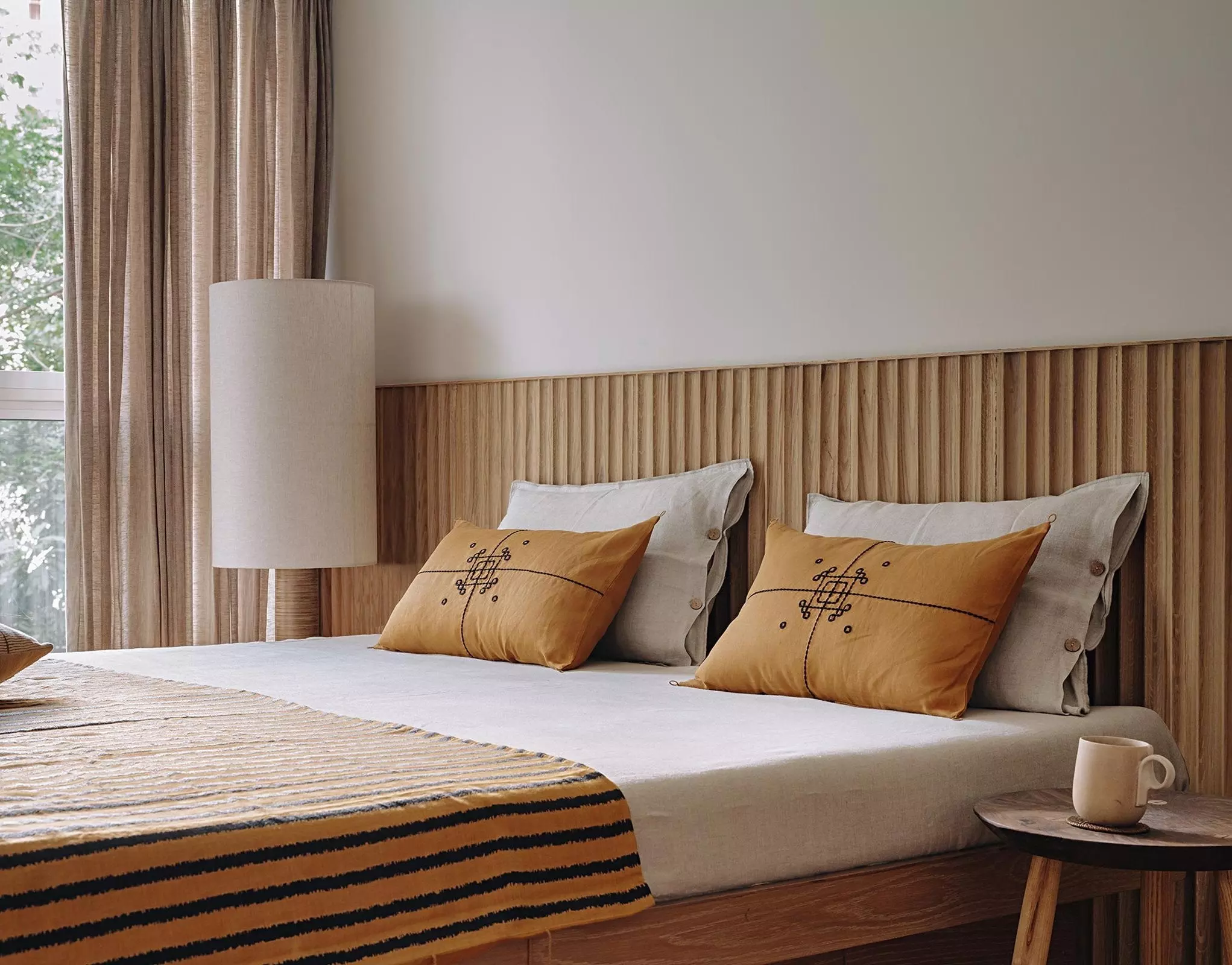 Image of Japandi bedroom with orange throw pillows, fluted wood wall panelling, and warmly colored bedding