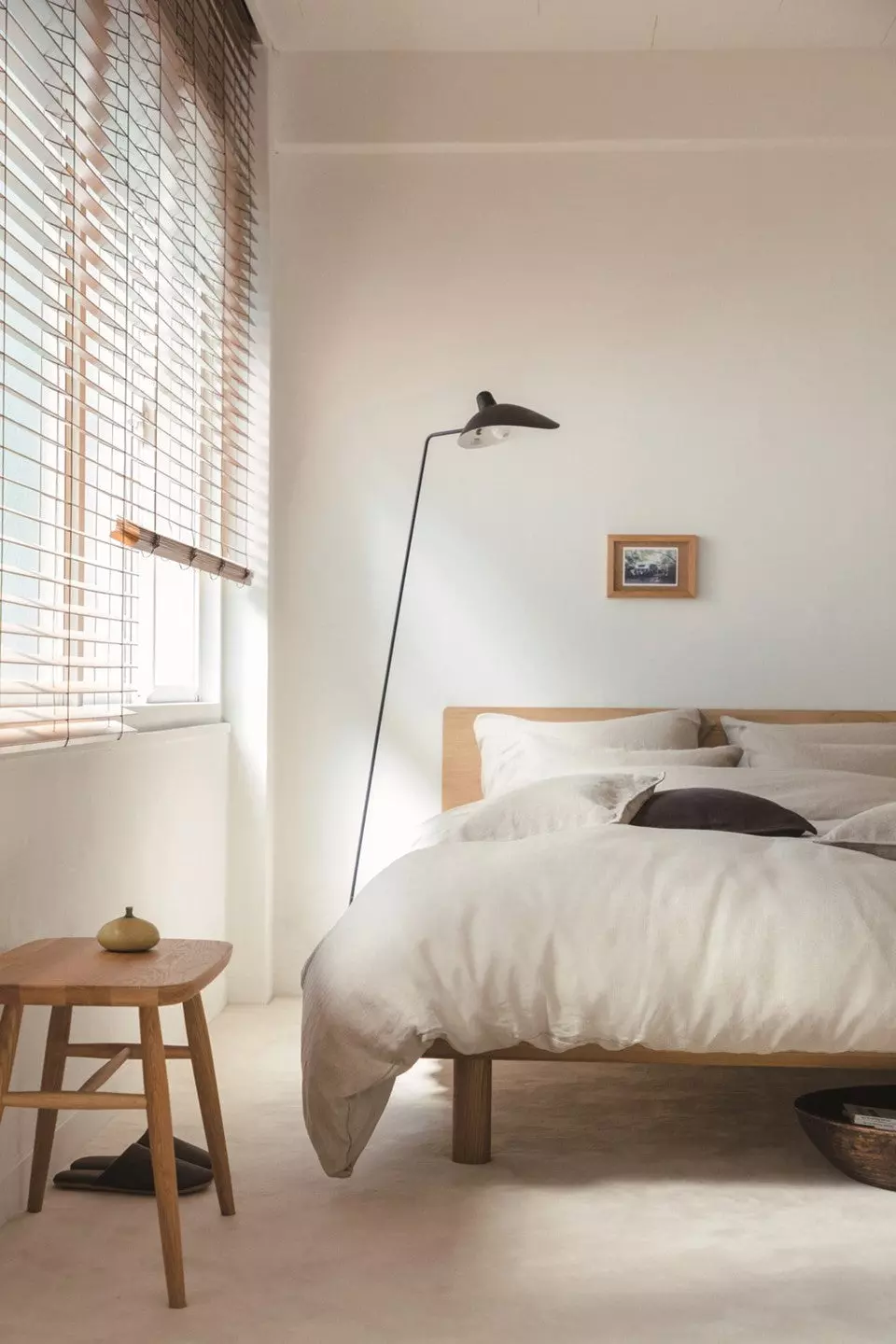 Image of a simple bedroom with a white oak bedframe and a black floor lamp