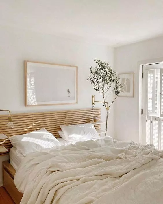 Image of a white bedroom with an indoor olive tree, framed art, and a slatted wood headboard