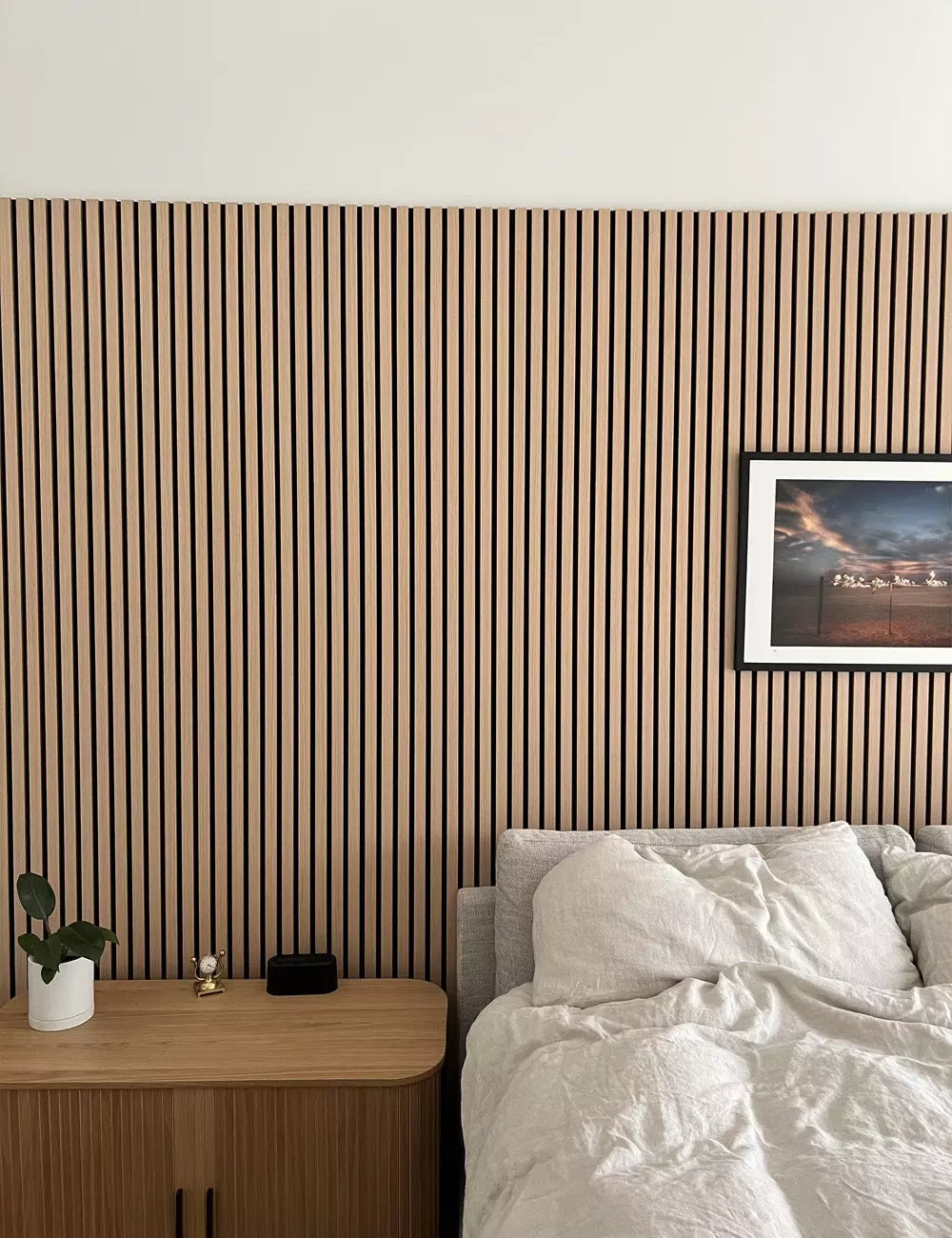 Image of a light Scandinavian bedroom with neutral bedding and a vertical wood slat accent wall behind the bed