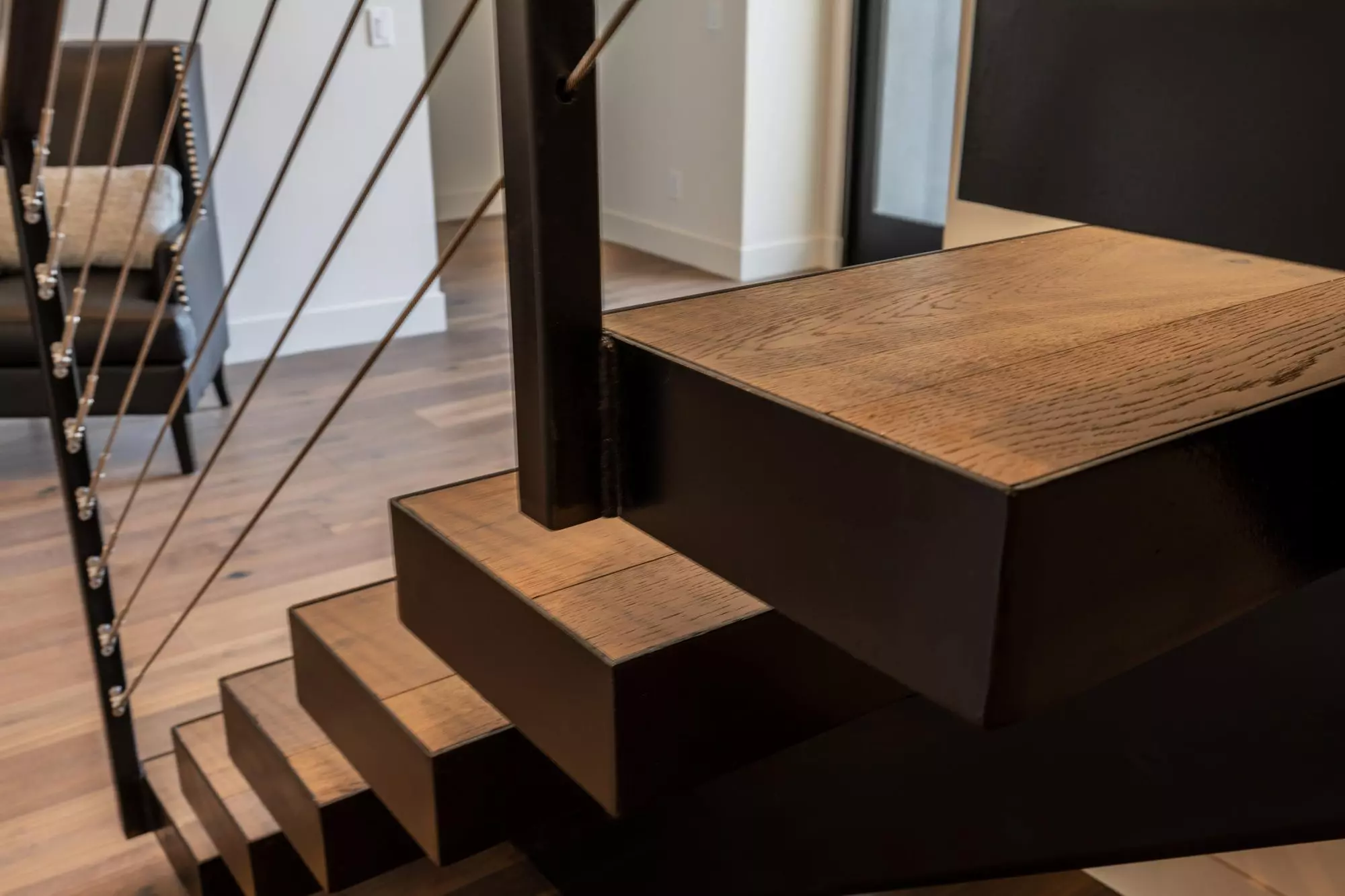 Closeup detail photo of a modern staircase. Open frame staircase with metal backbone and wood steps. Wire railings.