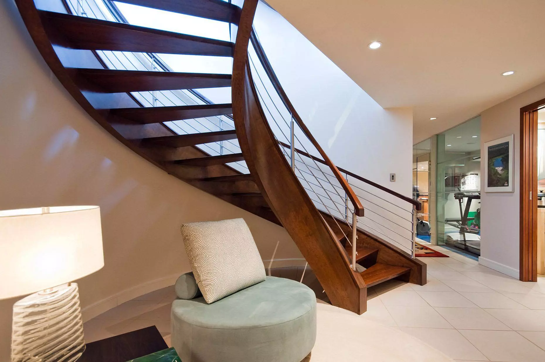 Sexy curved modern staircase design with real wood stained a medium brown. Open risers. Metal balusters with wood rail.