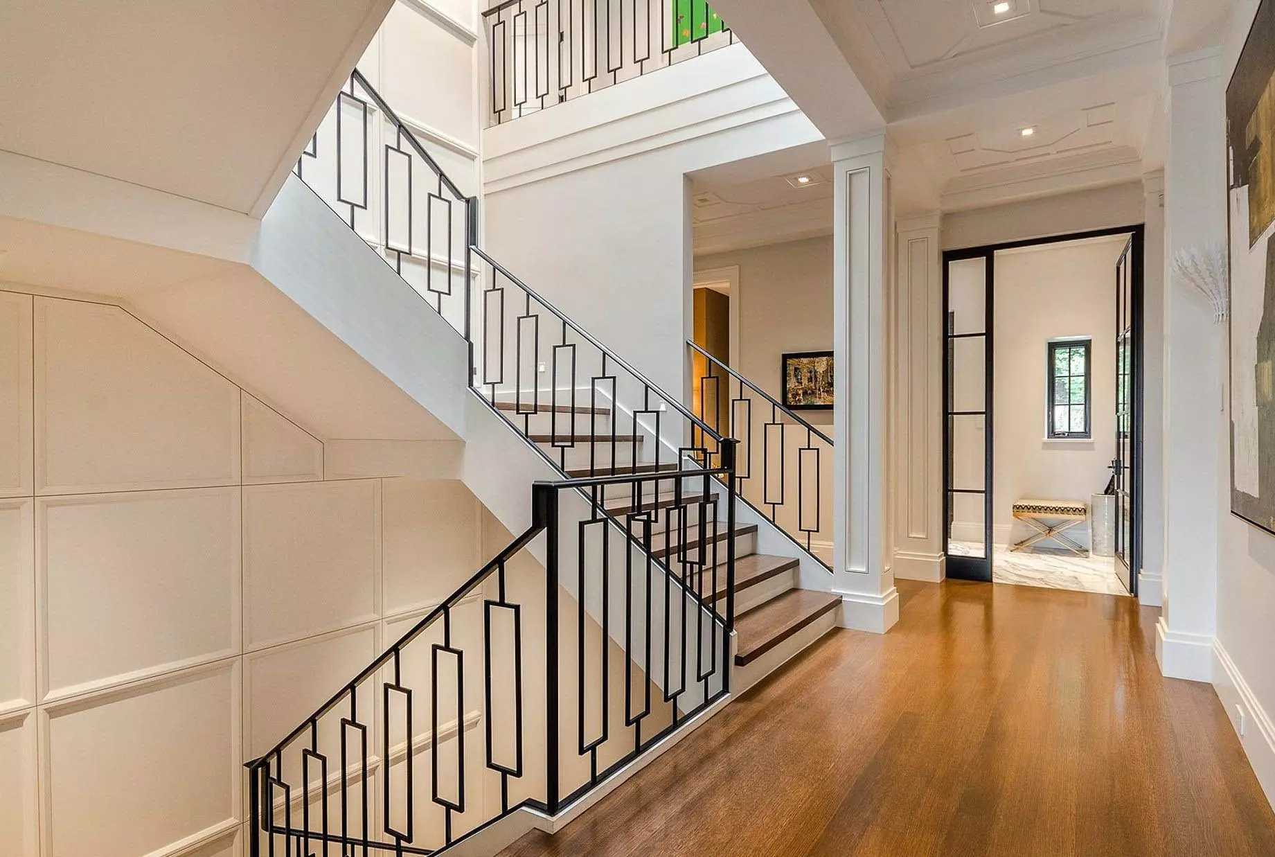 Transitional modern staircase design made with black iron. Custom wall paneling adorns the stair walls. Wood floors with white risers.