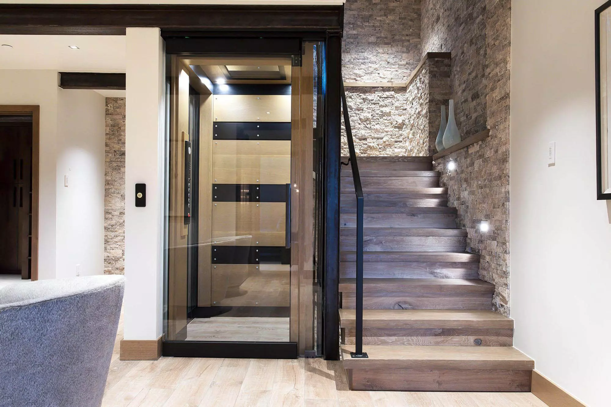 Beautiful modern staircase design featuring light gray wood and matching stone wall veneer. Black metal railings. Matching hardwood floors.