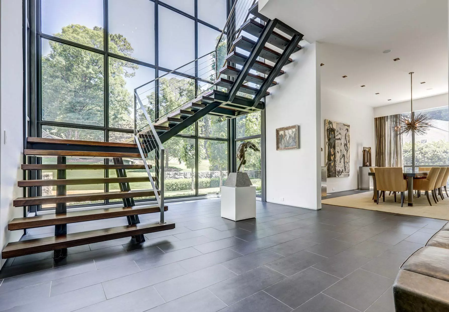 Modern metal and wood winding staircase with metal railings in front of a stunning 2-story glass wall.