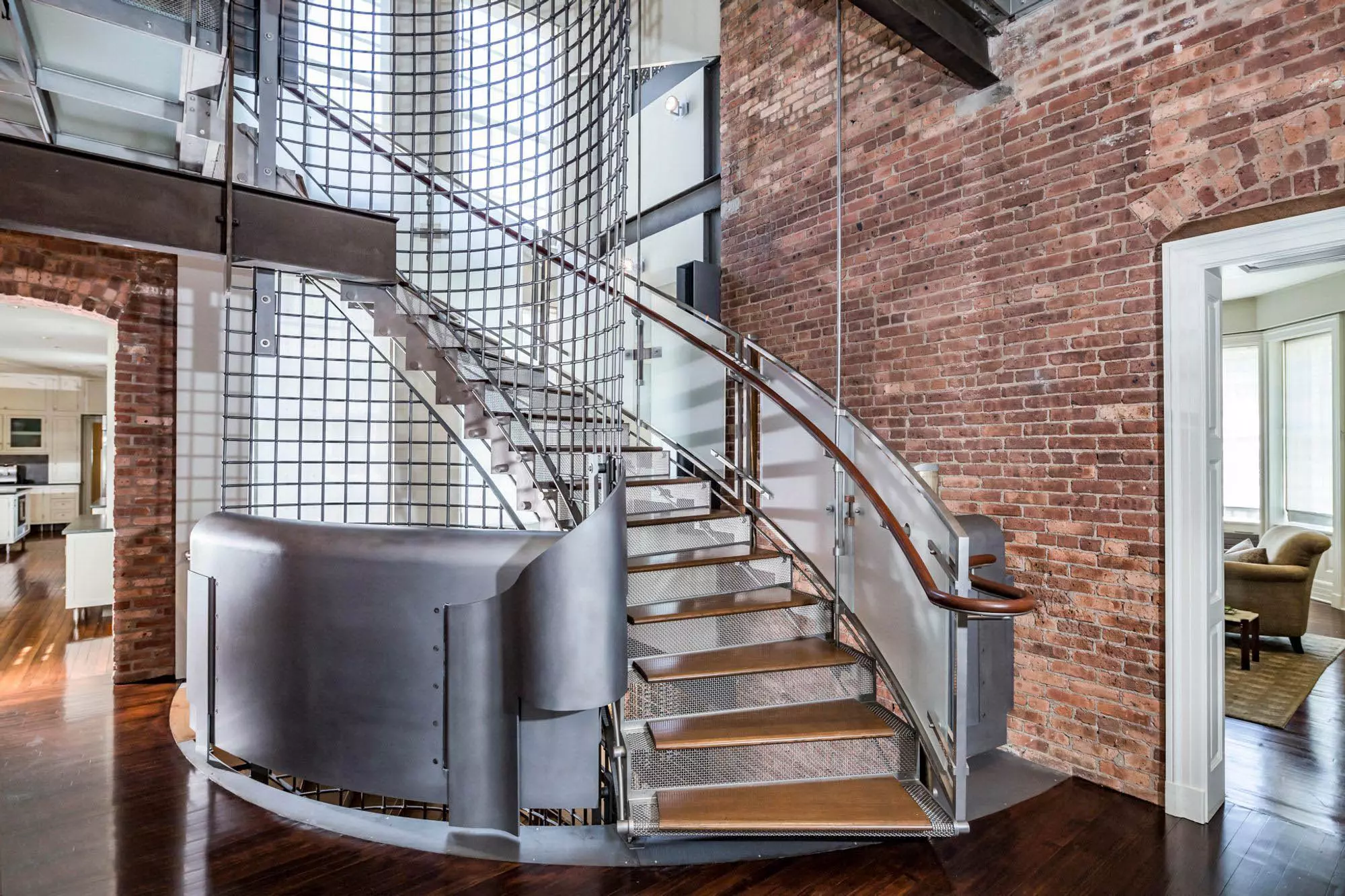 Modern industrial staircase design with aluminum, steel, wood, and glass. Red brick walls and dark-stained hardwood floors.