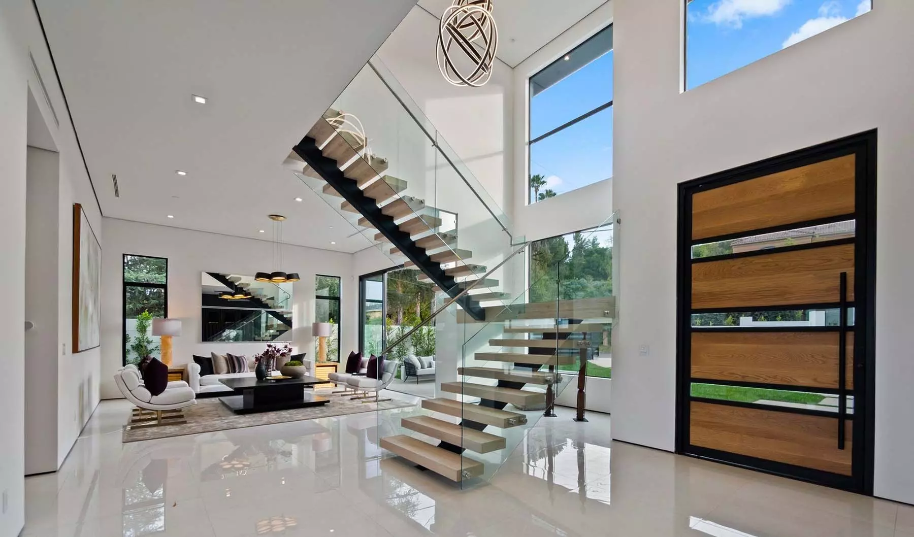 Modern staircase design with black metal backbone, wood steps, and glass railings.