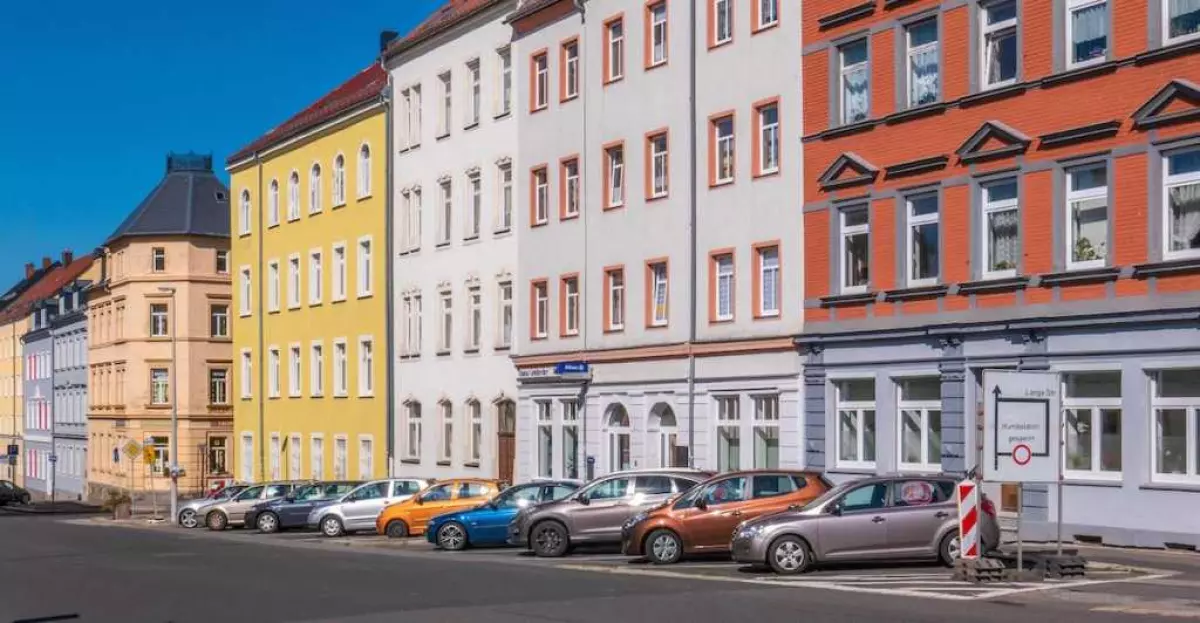 A row of colorful houses with an array of parked cars lining the street in front of it.