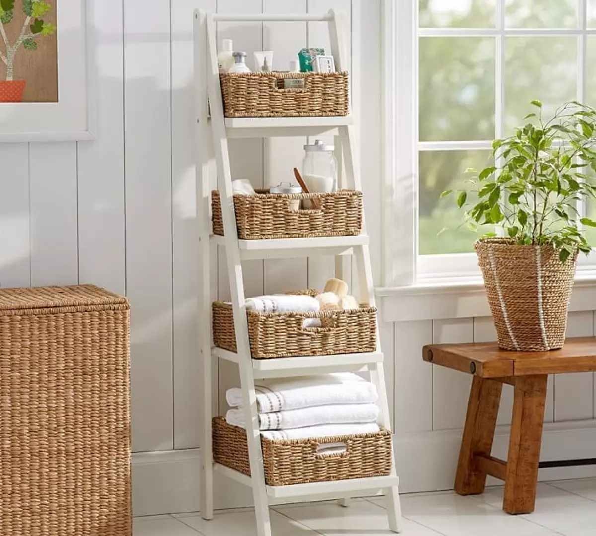 White ladder shelves filled with baskets and toiletries while leaning against a white wall.