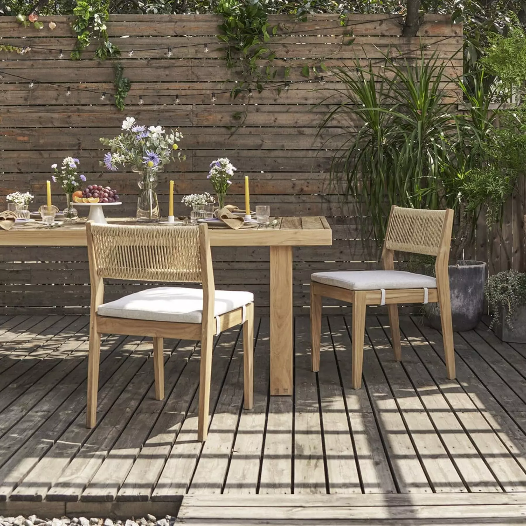 A teak outdoor dining table and 2 teak chairs with fabric cushions.