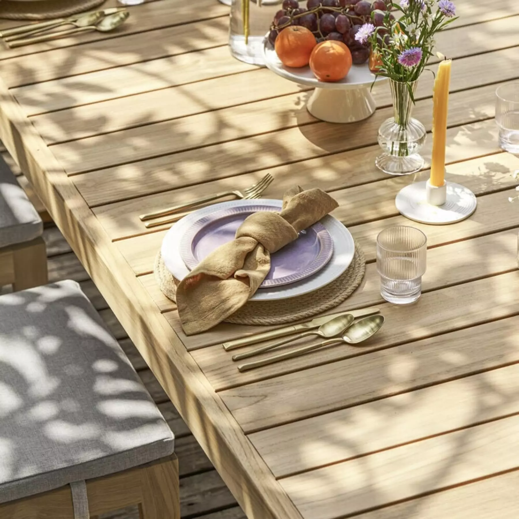 A teak outdoor dining table with cutlery and plates.