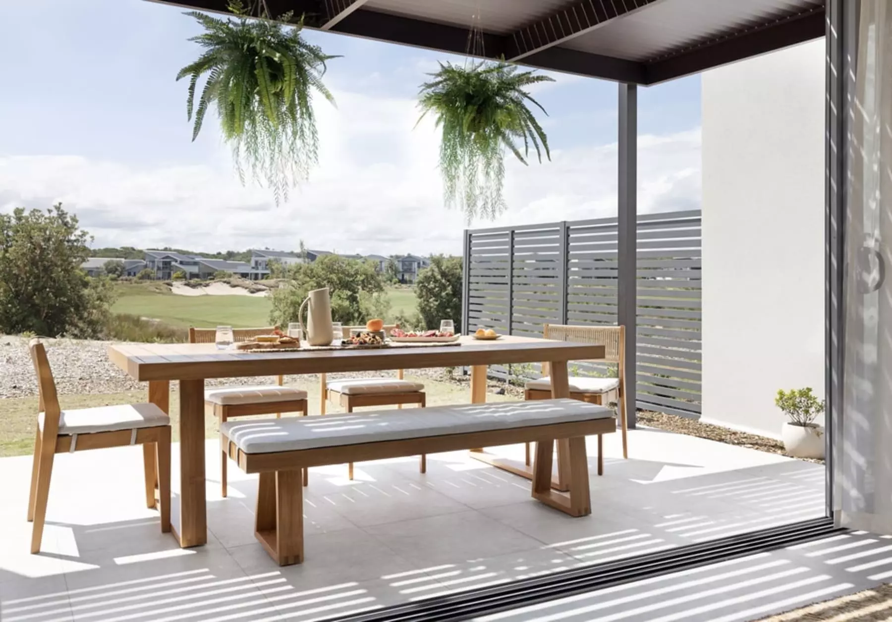 An outdoor teak dining table with 4 chairs and a bench.