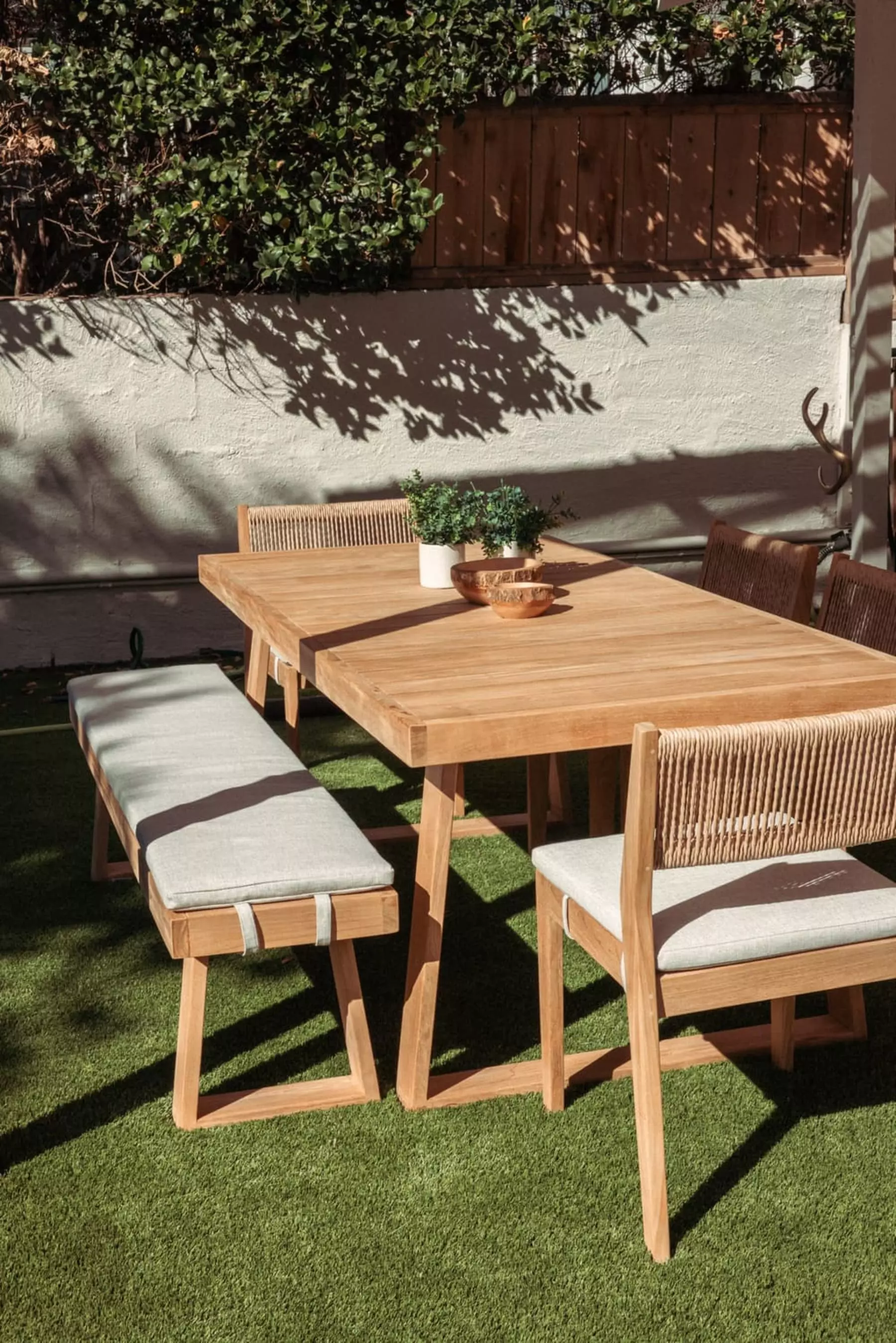 A teak outdoor dining table and bench basking in the sunlight.