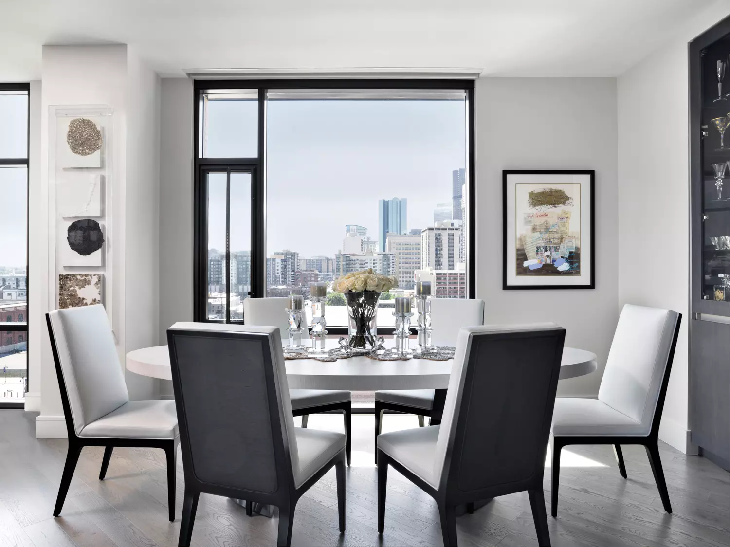 dining room with glossy oval table and six white leather chairs, with two artworks on wall