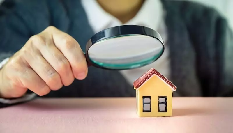 A person using a laptop for property searches and holding a magnifying glass, indicating an in-depth investigation