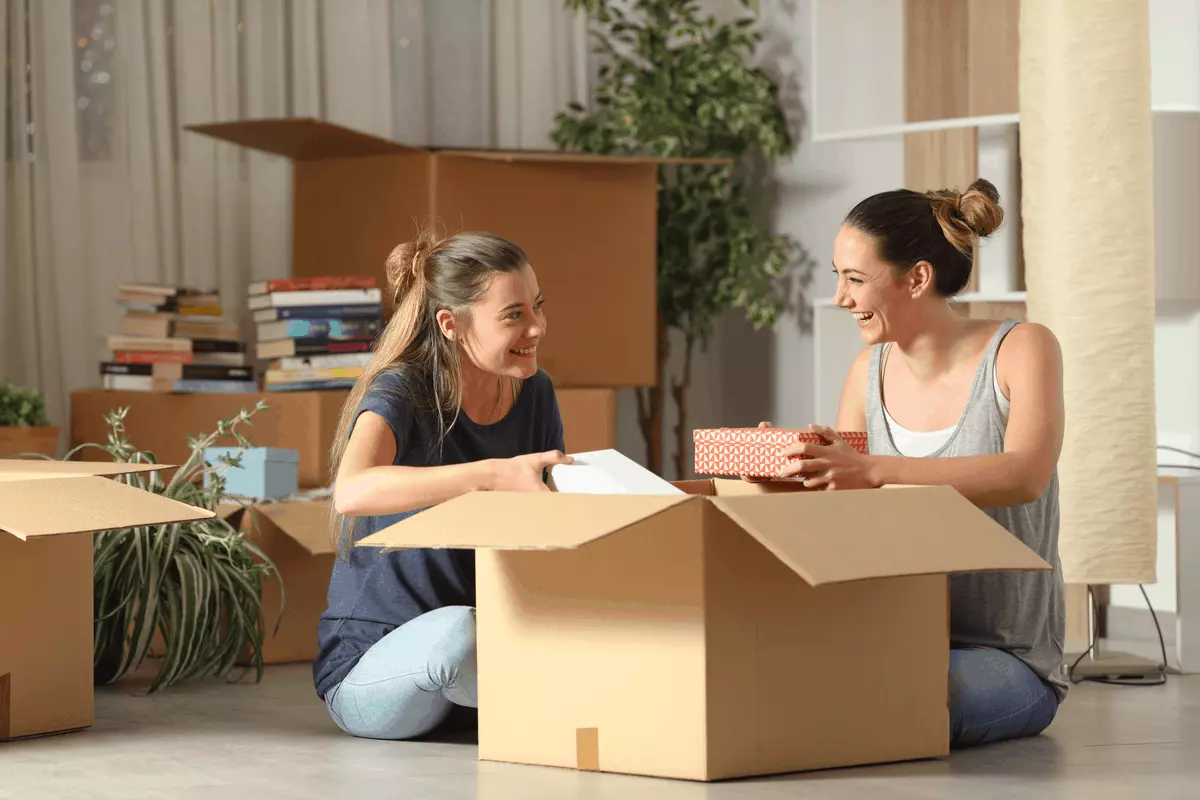 Two women unpacking a box in an apartment.